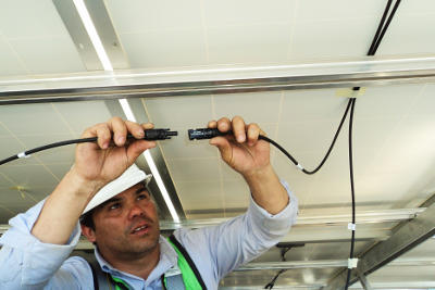 Obraz przedstawia robotnika łączącego przewody elektryczne pod sufitem